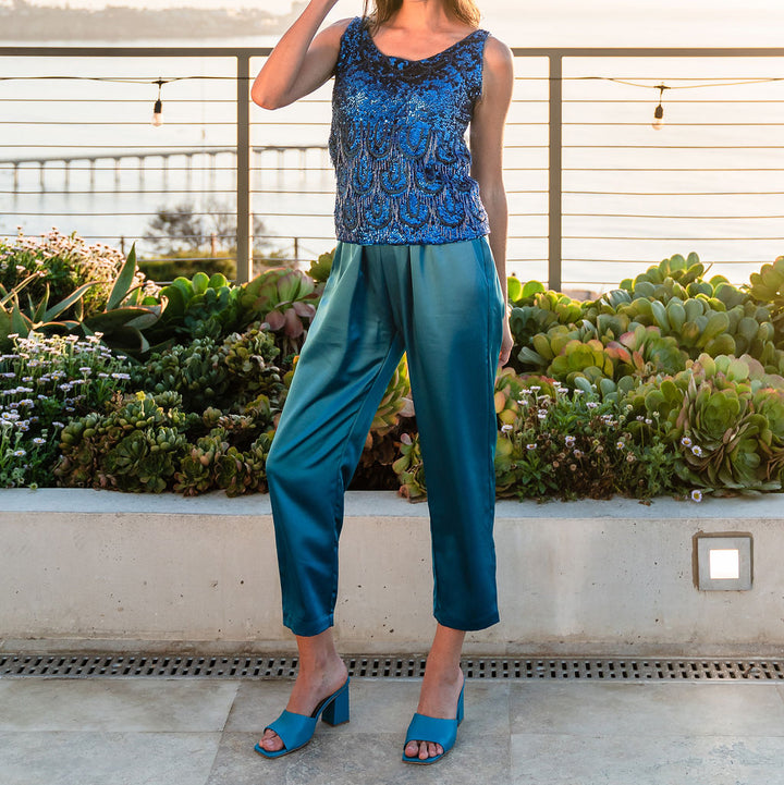Woman in blue top and pants standing on a rooftop with greenery