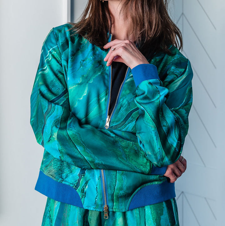Woman wearing a green jacket and sunglasses against a white wall.