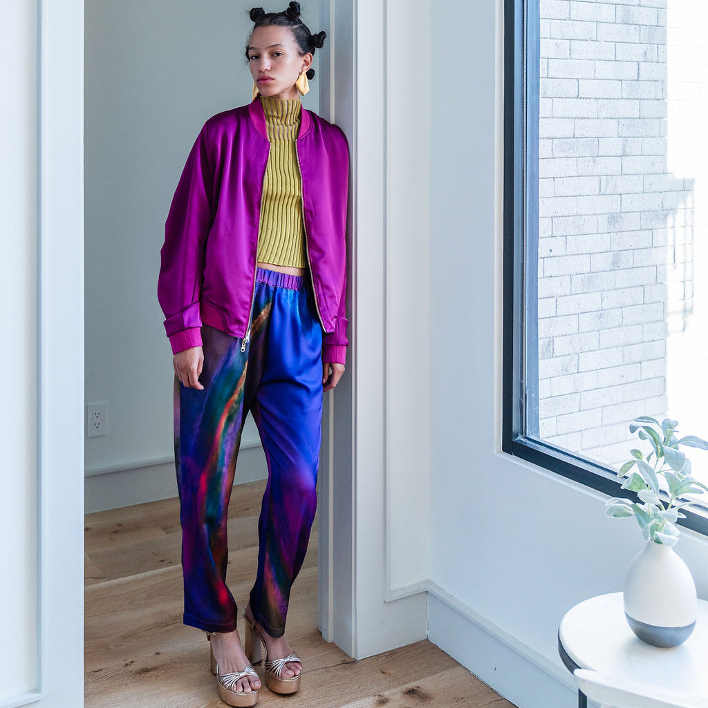 Person wearing a bright pink jacket and colorful pants standing in a room with a large window.