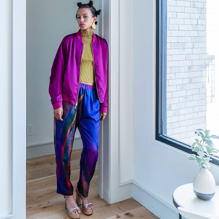 Person wearing a bright pink jacket and colorful pants standing in a room with a large window.