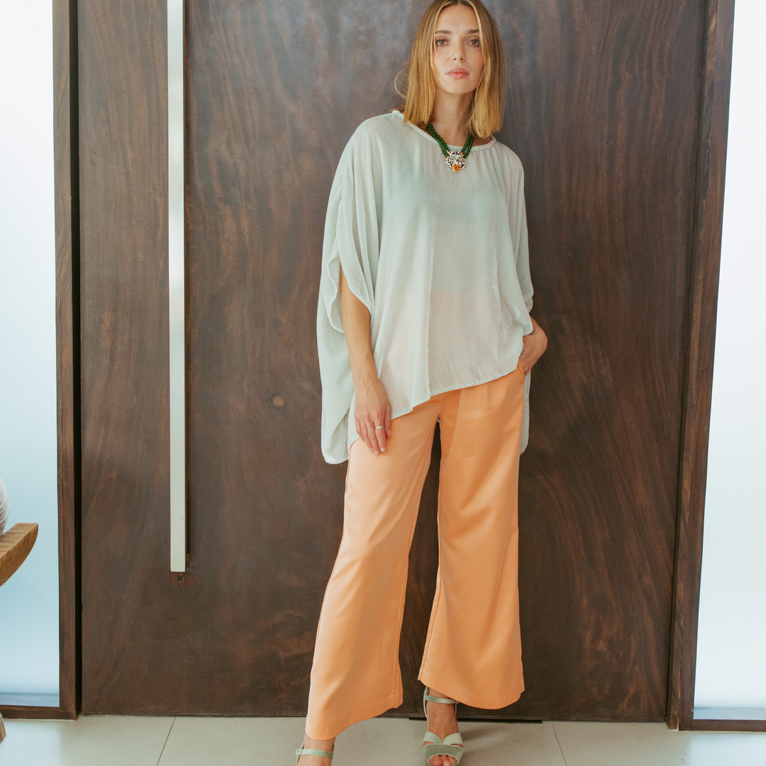 Woman wearing a light-colored top and peach pants standing against a wooden wall.