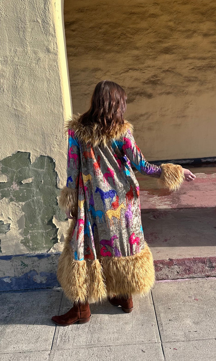 Person wearing a colorful coat with fur trim standing against a wall.