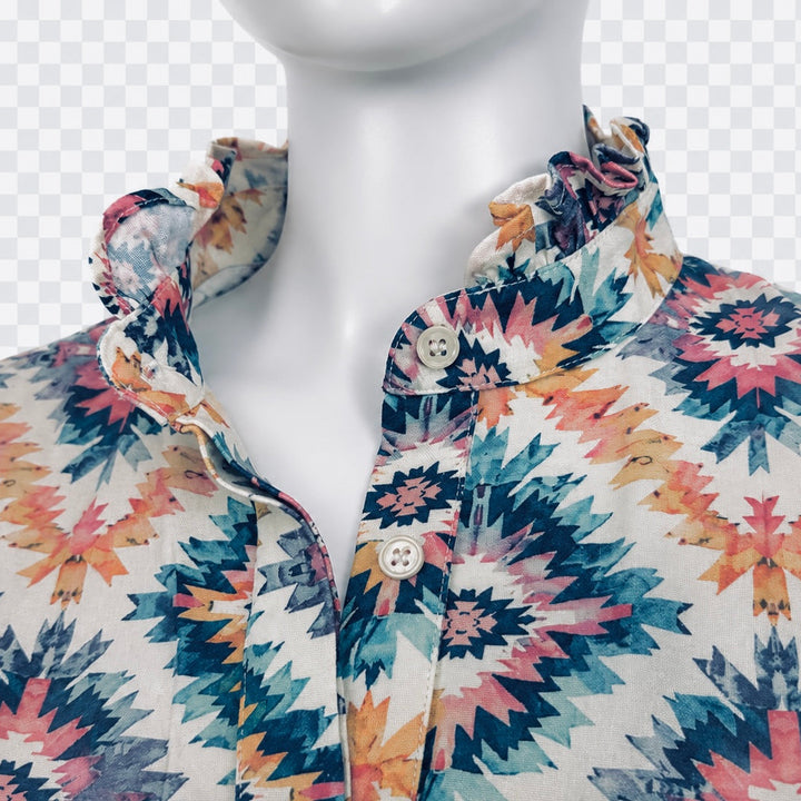 A close-up of a white mannequin torso wearing a collared button-front shirt with a colorful geometric southwestern-style print in teal, pink, orange, and cream on a checkered background.