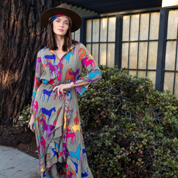 Woman wearing a colorful patterned dress and brown boots standing outdoors.