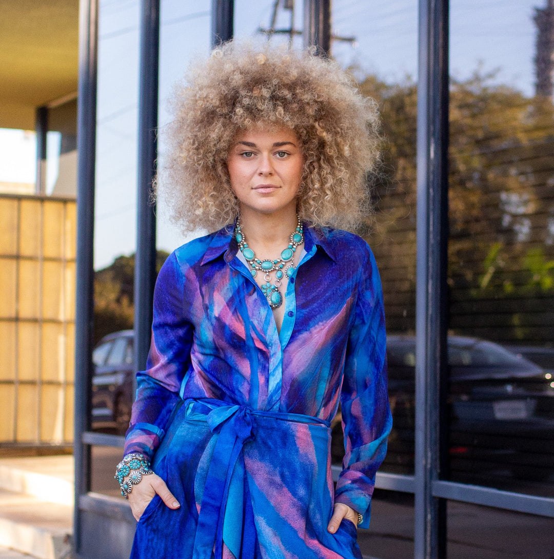 Woman in a blue dress standing outside a building with large windows.