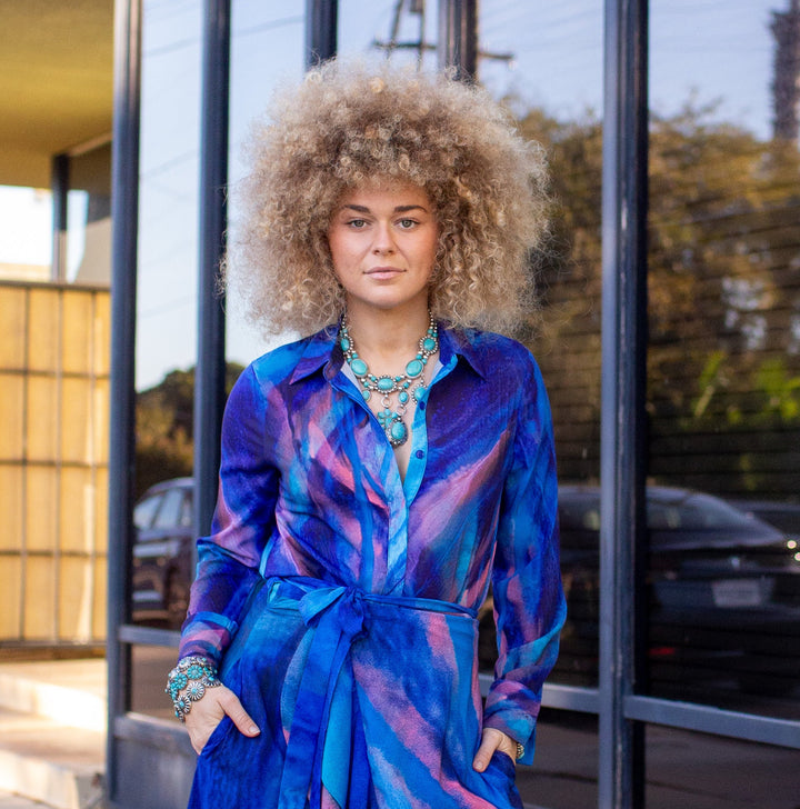 Woman in a blue dress standing outside a building with large windows.