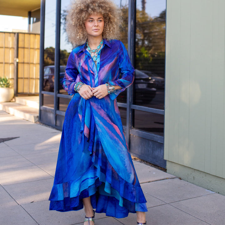 Woman in a blue dress standing outside a building with large windows.