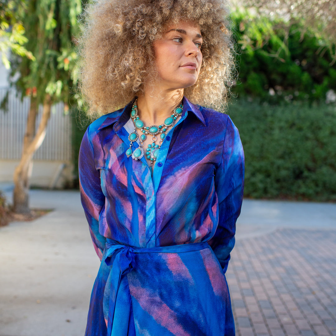 Woman wearing a colorful dress with a tie at the waist, standing outdoors.