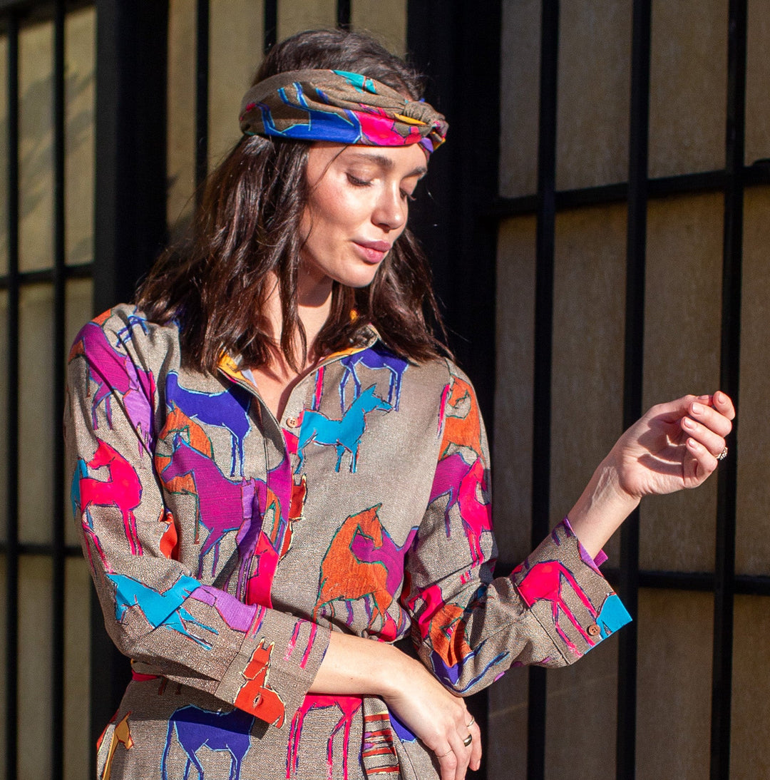 Woman wearing a colorful dress with animal prints standing on a sidewalk.