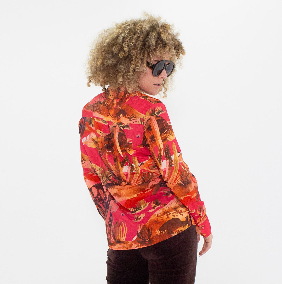 Person wearing a colorful blouse and dark flared pants on a white background