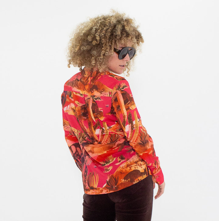 Person wearing a colorful blouse and dark flared pants on a white background