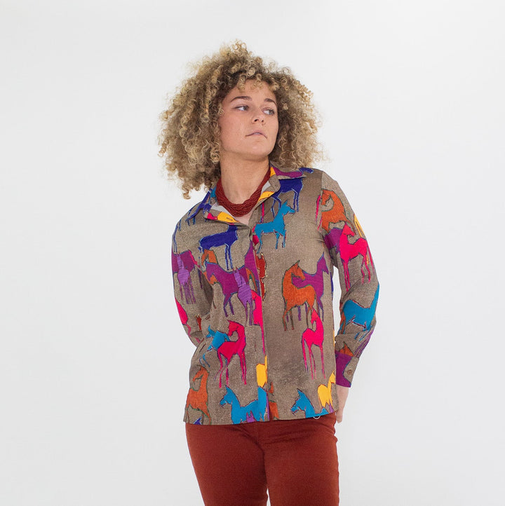 Person wearing a colorful blouse with animal patterns and red pants on a white background