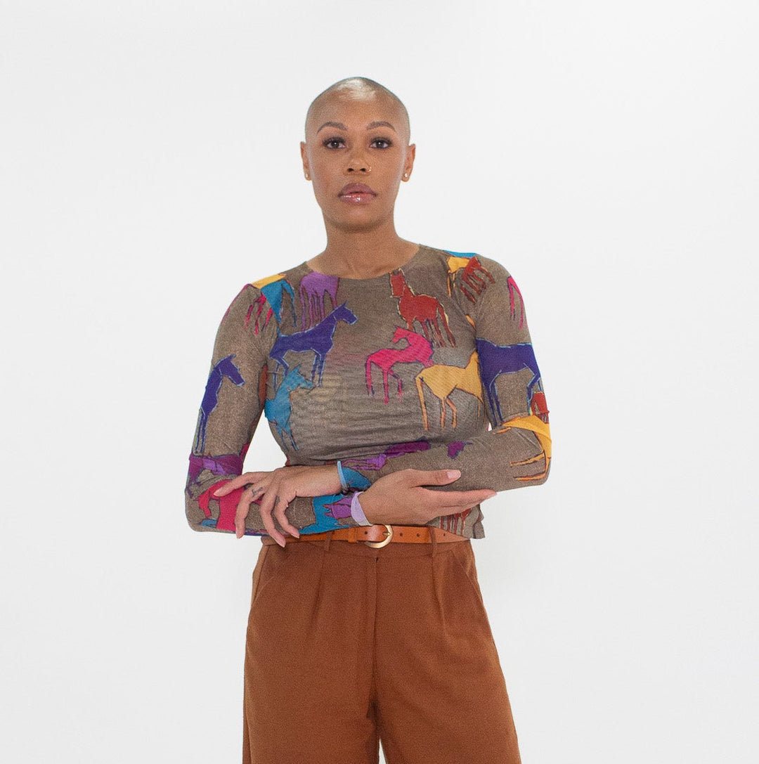 Person wearing a colorful top with horse prints and brown wide-leg pants on a white background