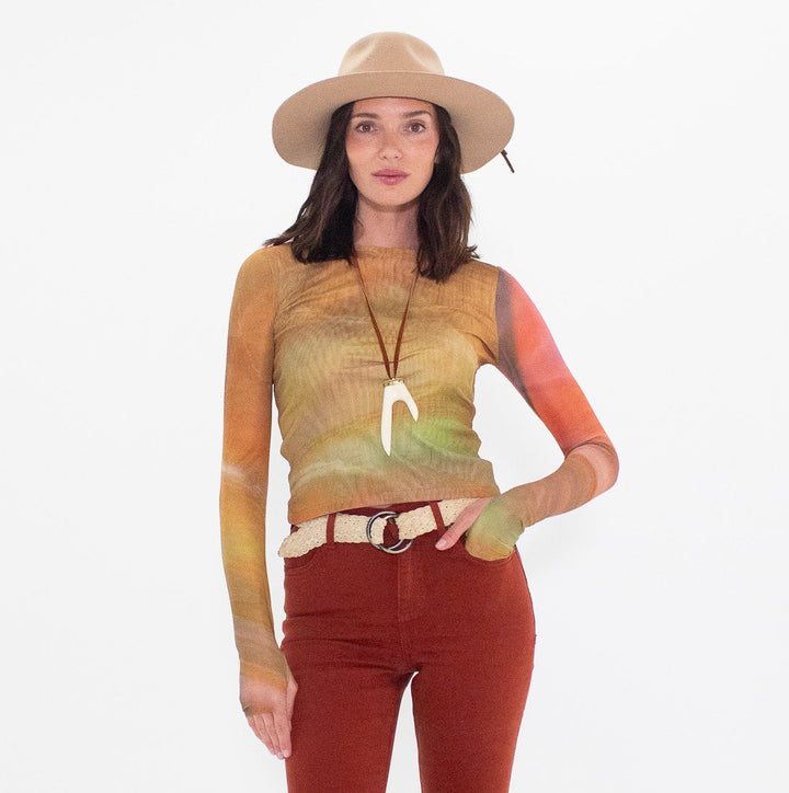 Woman wearing a long sleeve top with a colorful design and rust flared pants on a white background