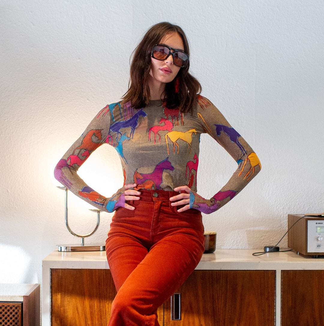 Woman wearing a colorful horse print top and red pants in an indoor setting.