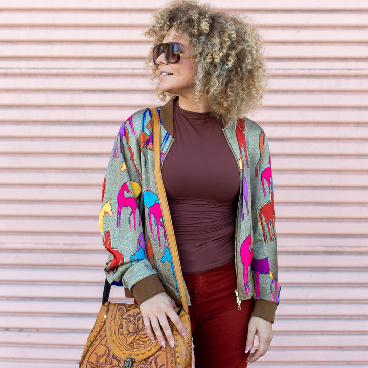 Woman wearing a colorful jacket, brown top, red pants, and sunglasses against a pink wall.