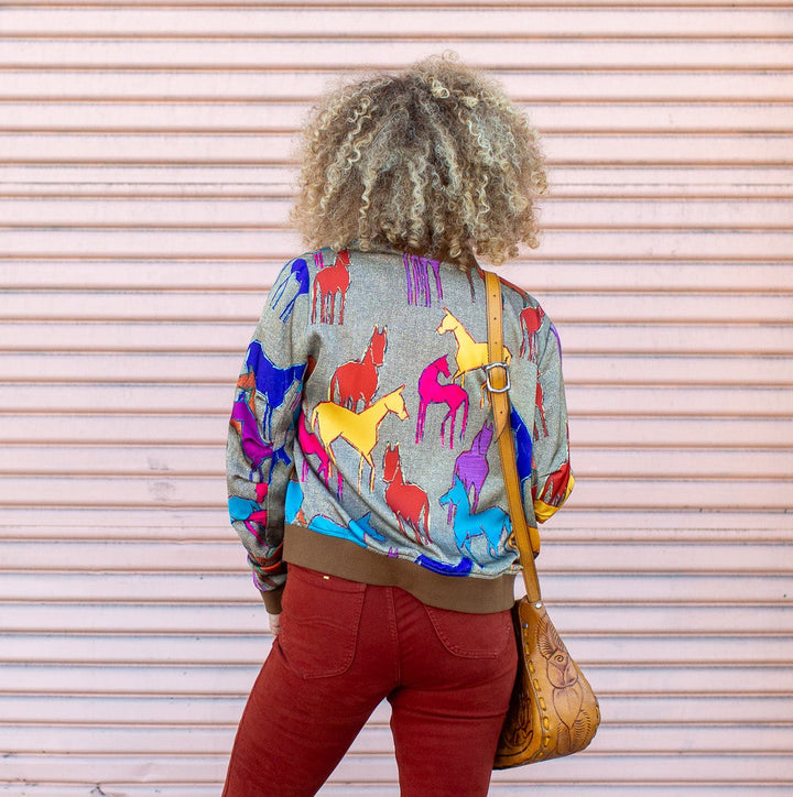 Person wearing a colorful jacket and red pants standing in front of a pink wall.